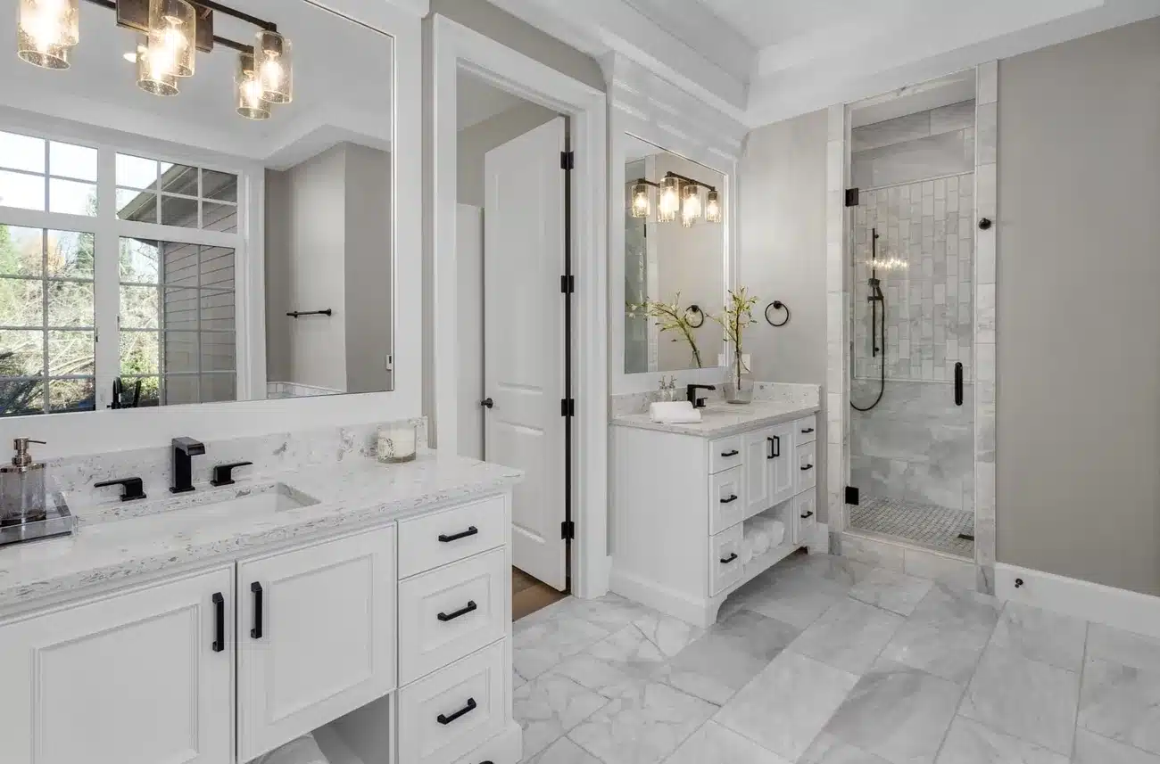 Bright modern bathroom with white cabinetry, marble non-slip tile flooring, and a glass shower enclosure.