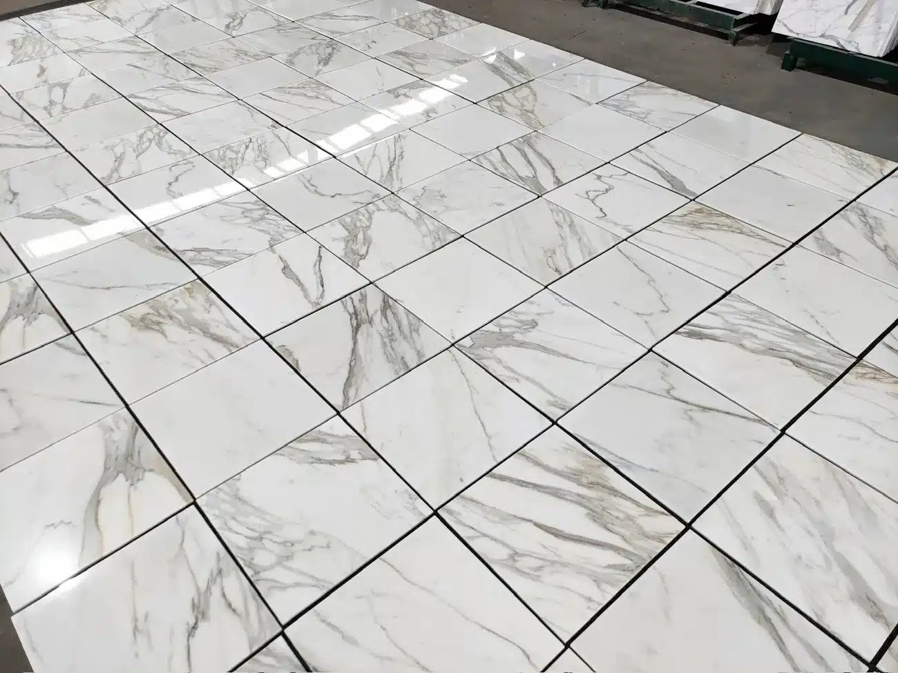 Glossy 18x18 Calacatta Gold marble tiles with white background and gold-gray veining arranged on floor.