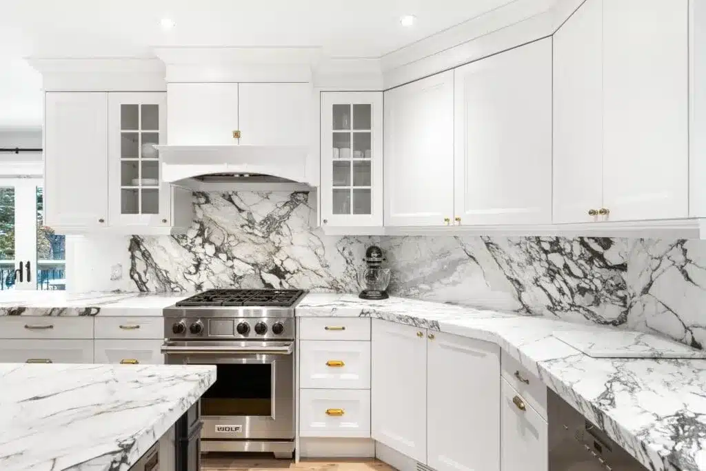 Bright kitchen with white cabinets and striking marble countertops and backsplash featuring bold gray veining.