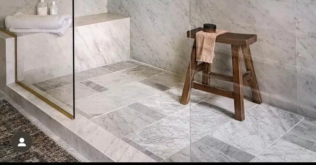 Marble shower floor and walls with epoxy grout, featuring a wooden stool and glass shower partition.