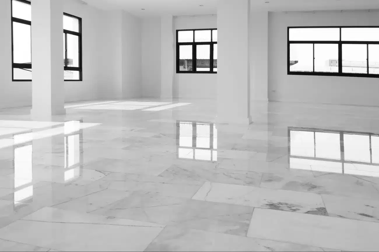 Empty room with polished white marble floors reflecting large windows and pillars, showcasing heated flooring comfort.