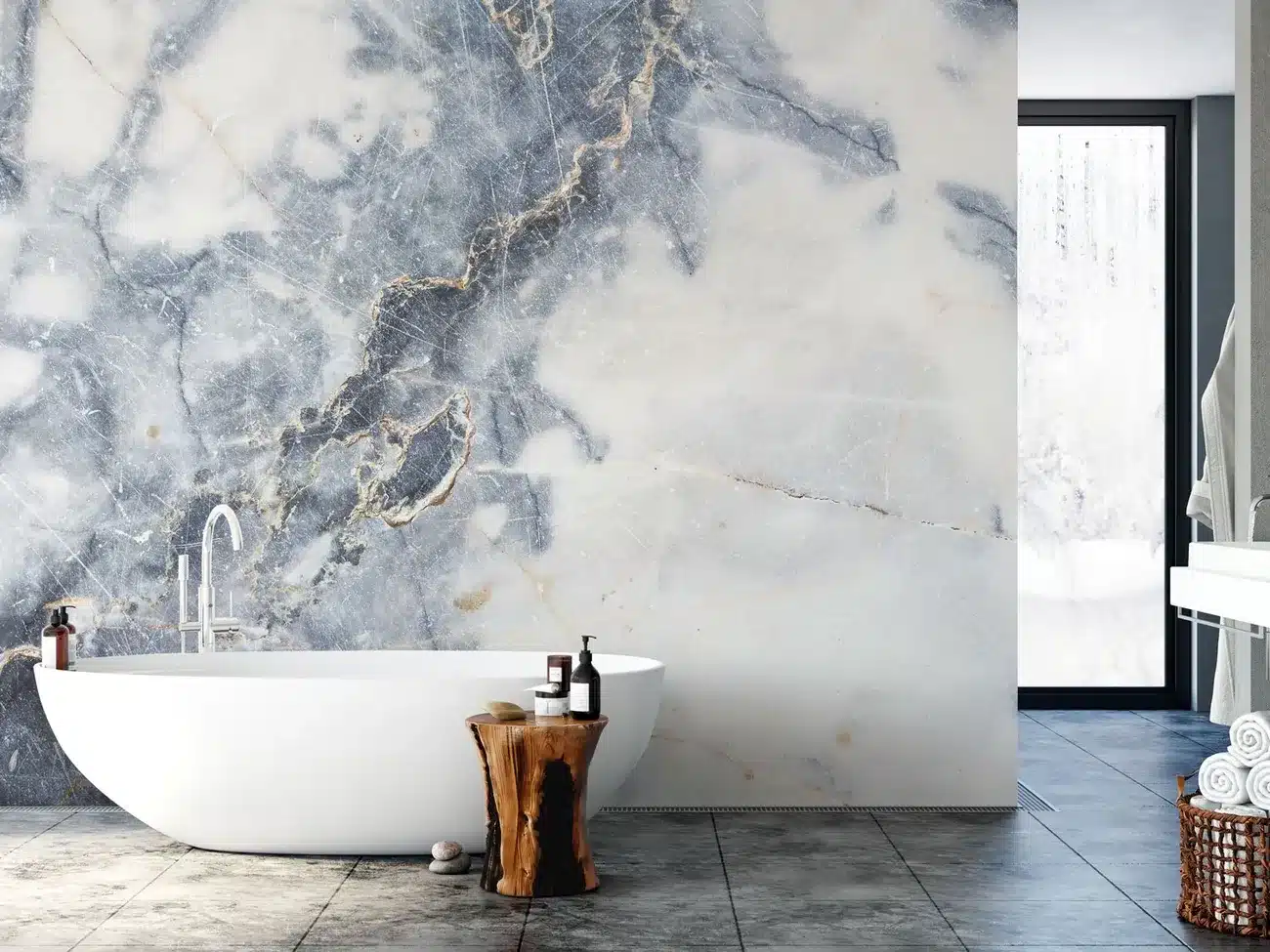 Modern bathroom with large marble accent wall, freestanding white tub, wooden side table, and gray floor tiles.